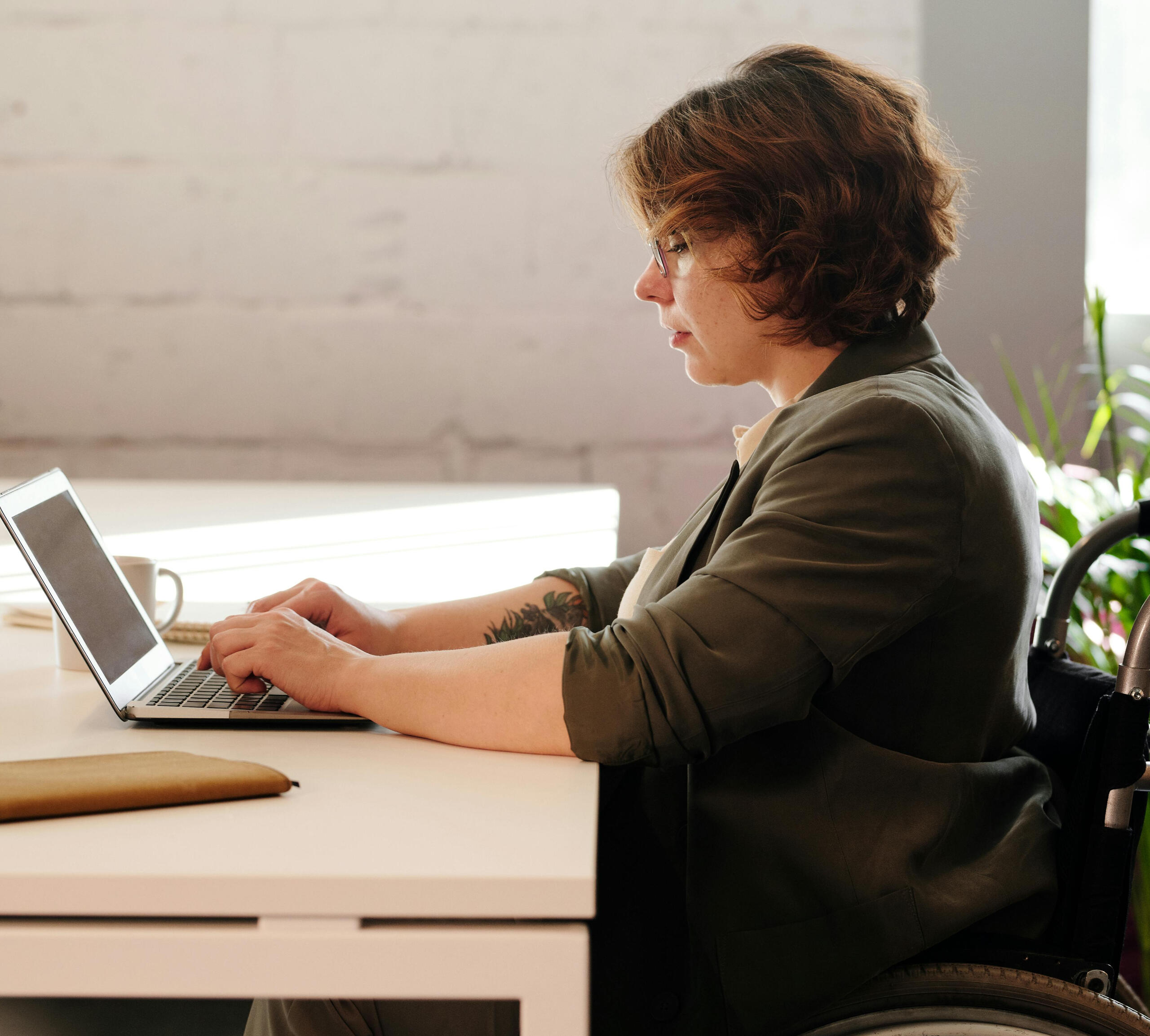 Dark haired woman in a wheelchair working at a white desk on a computer